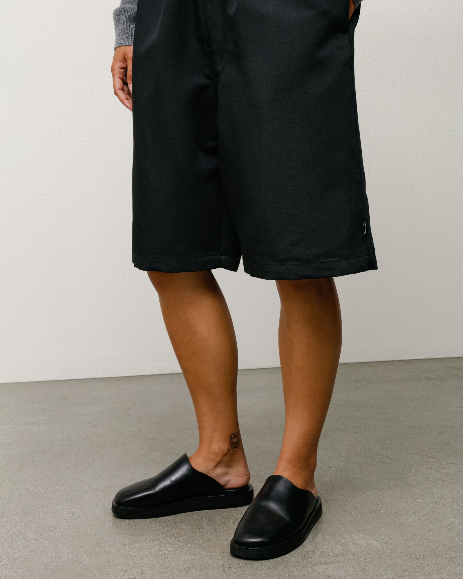 Black Baggy Beach Short on model, relaxed knee-length fit with clean hem and subtle side tag.