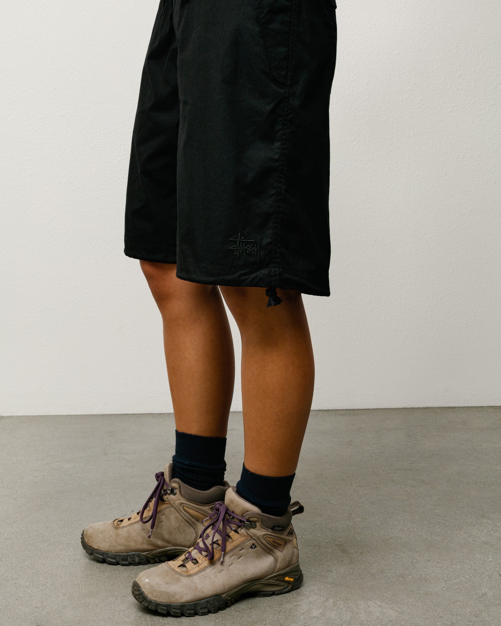 Black unisex knee-length surplus shorts with Stüssy logo embroidery at the hem, regular fit.