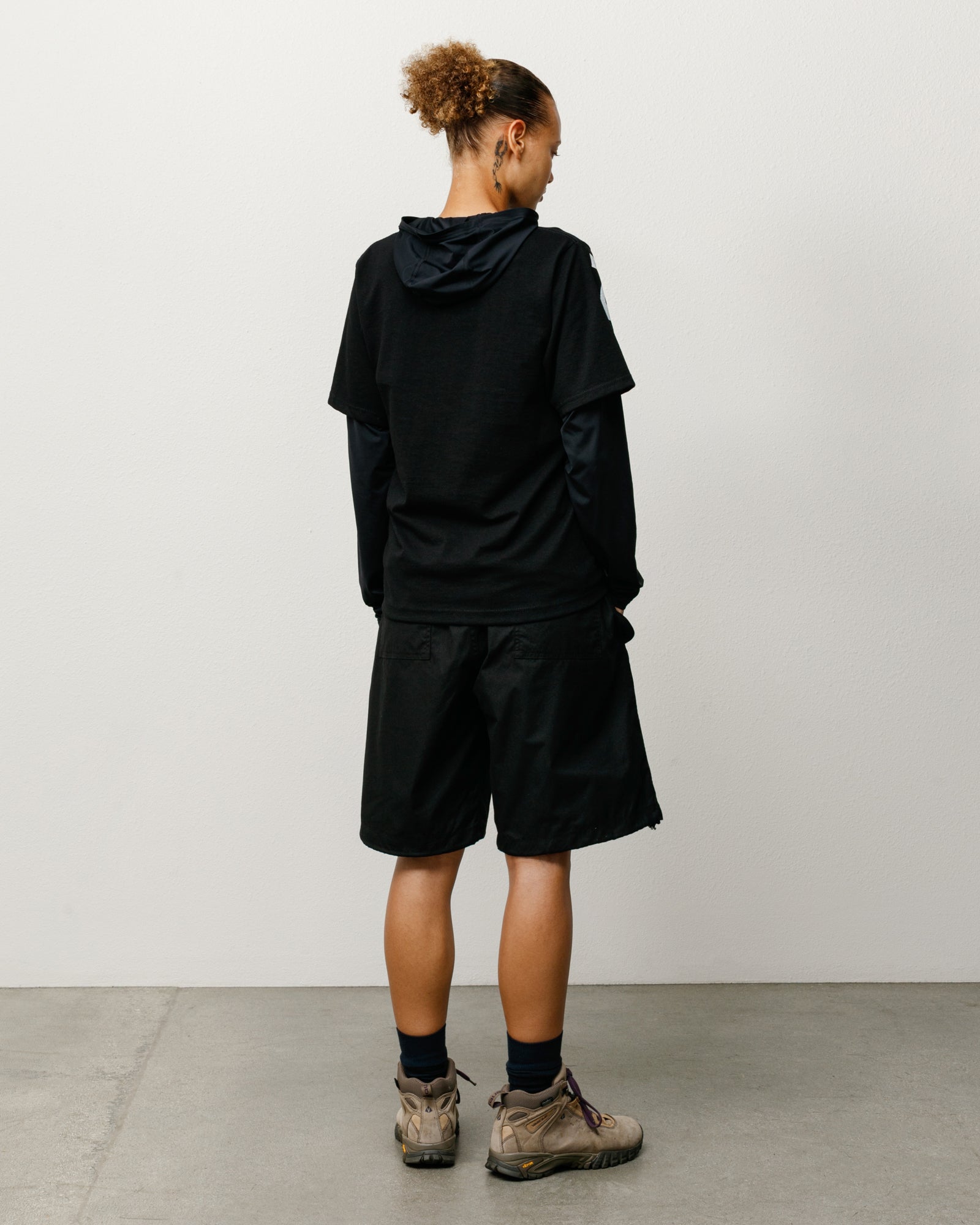 Black surplus shorts on model, unisex regular fit with rear patch pockets; back view.