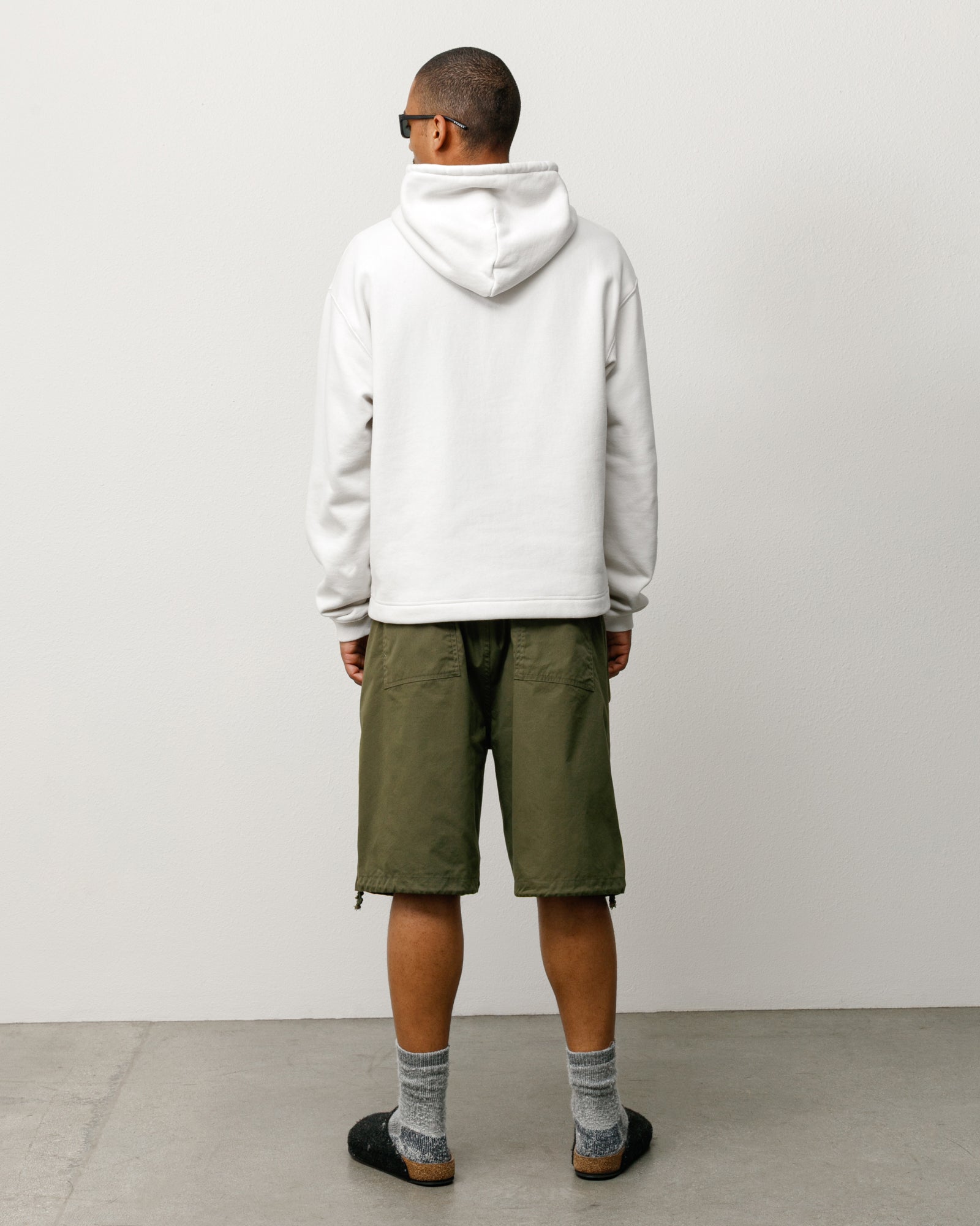 Olive surplus shorts, back view on model; baggy fit with rear patch pockets and drawcord hems.