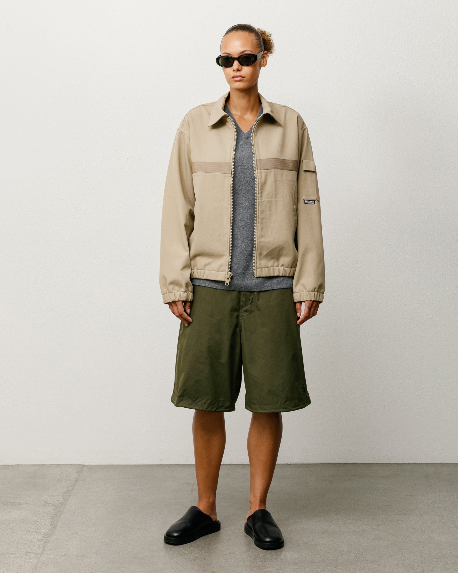 Olive baggy shorts on model, cotton-nylon, styled with grey tee, tan zip jacket and black slides