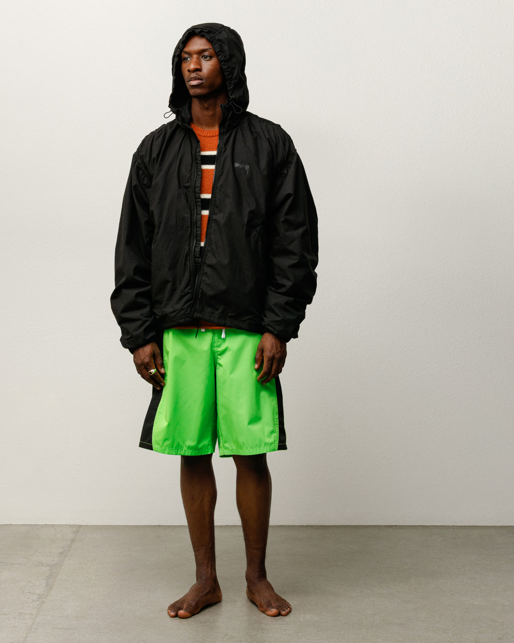 Male model wearing the Curved Panel Board Short in Green with the Double Cotton Hooded Jacket in Black.