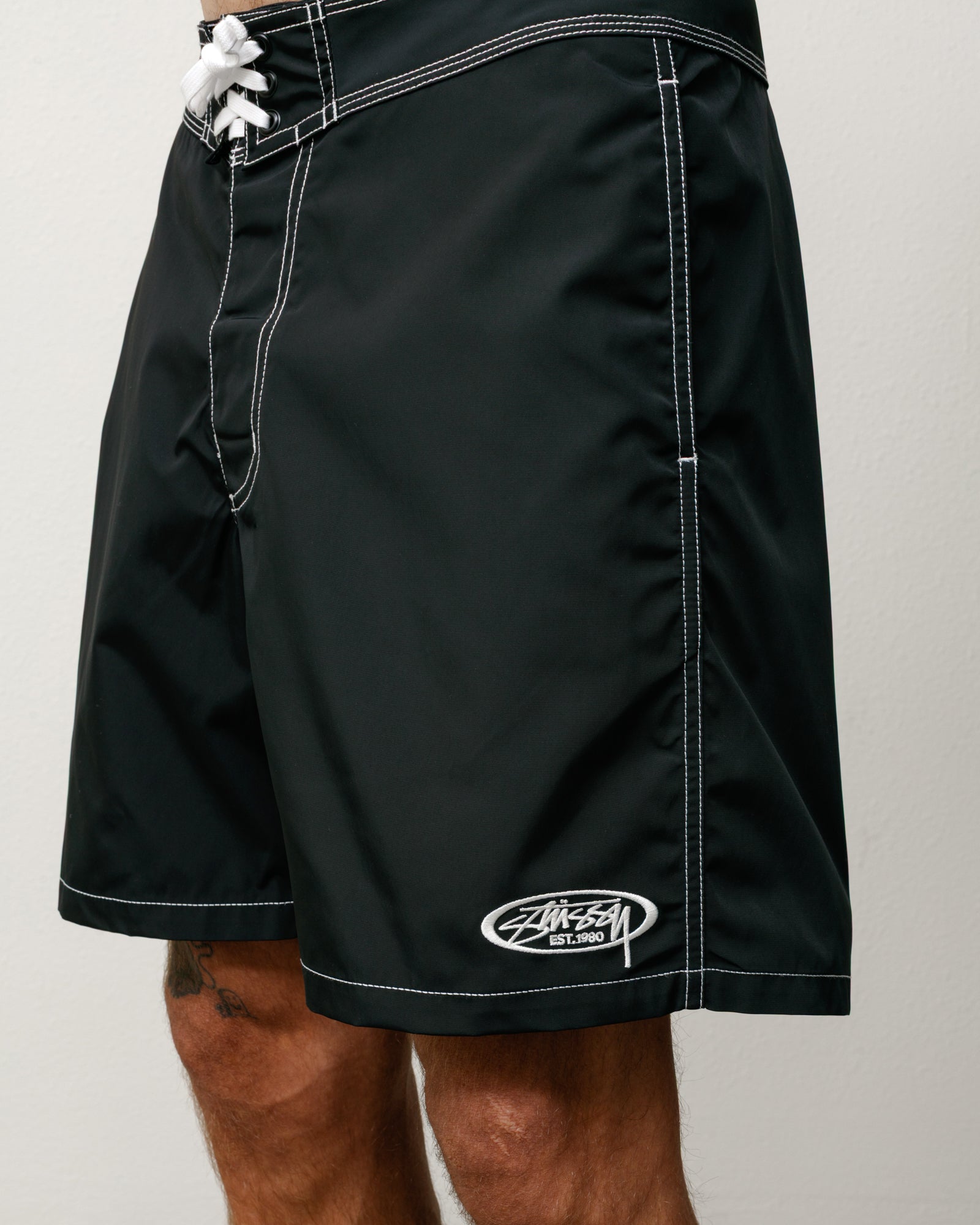 Black board short with white contrast stitching, lace-up waist, and Stüssy logo embroidery at left leg