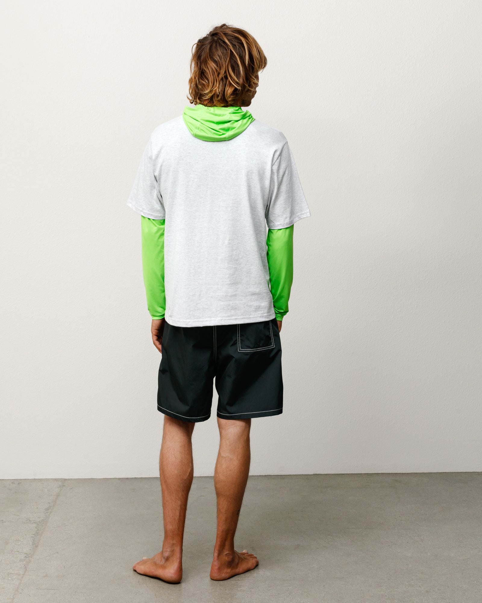 Black unisex board shorts on model, back view showing contrast stitching and rear patch pocket