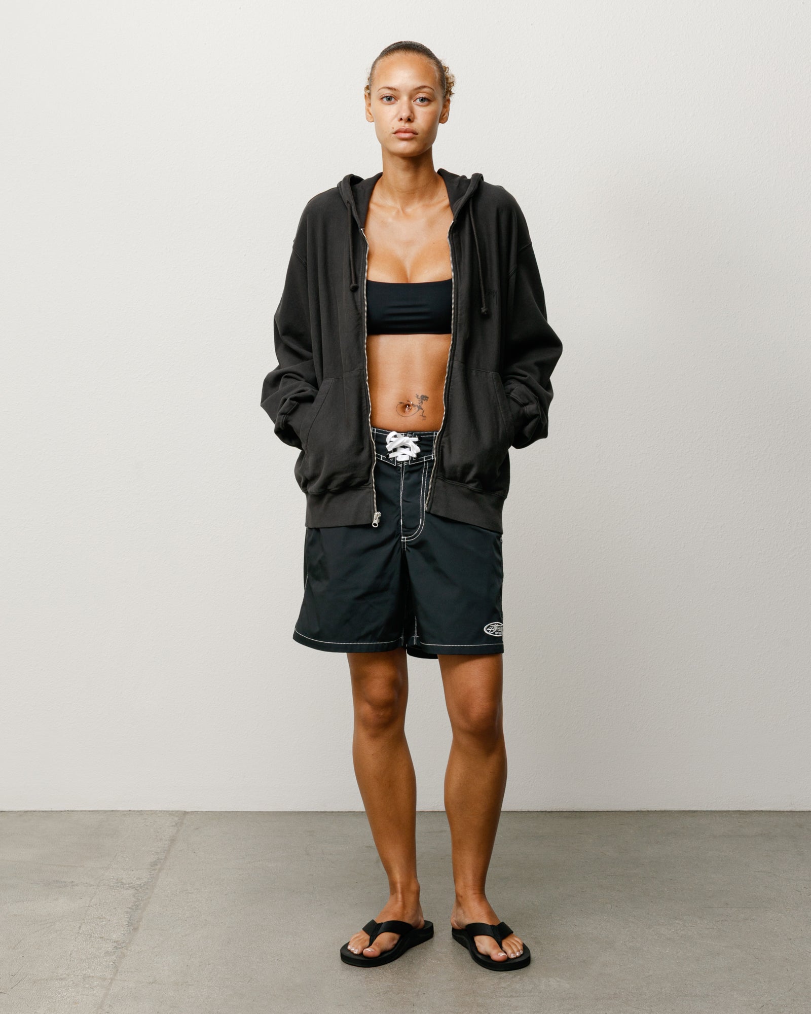 Black board shorts with white drawcord and contrast stitching, worn with a hoodie and sandals.