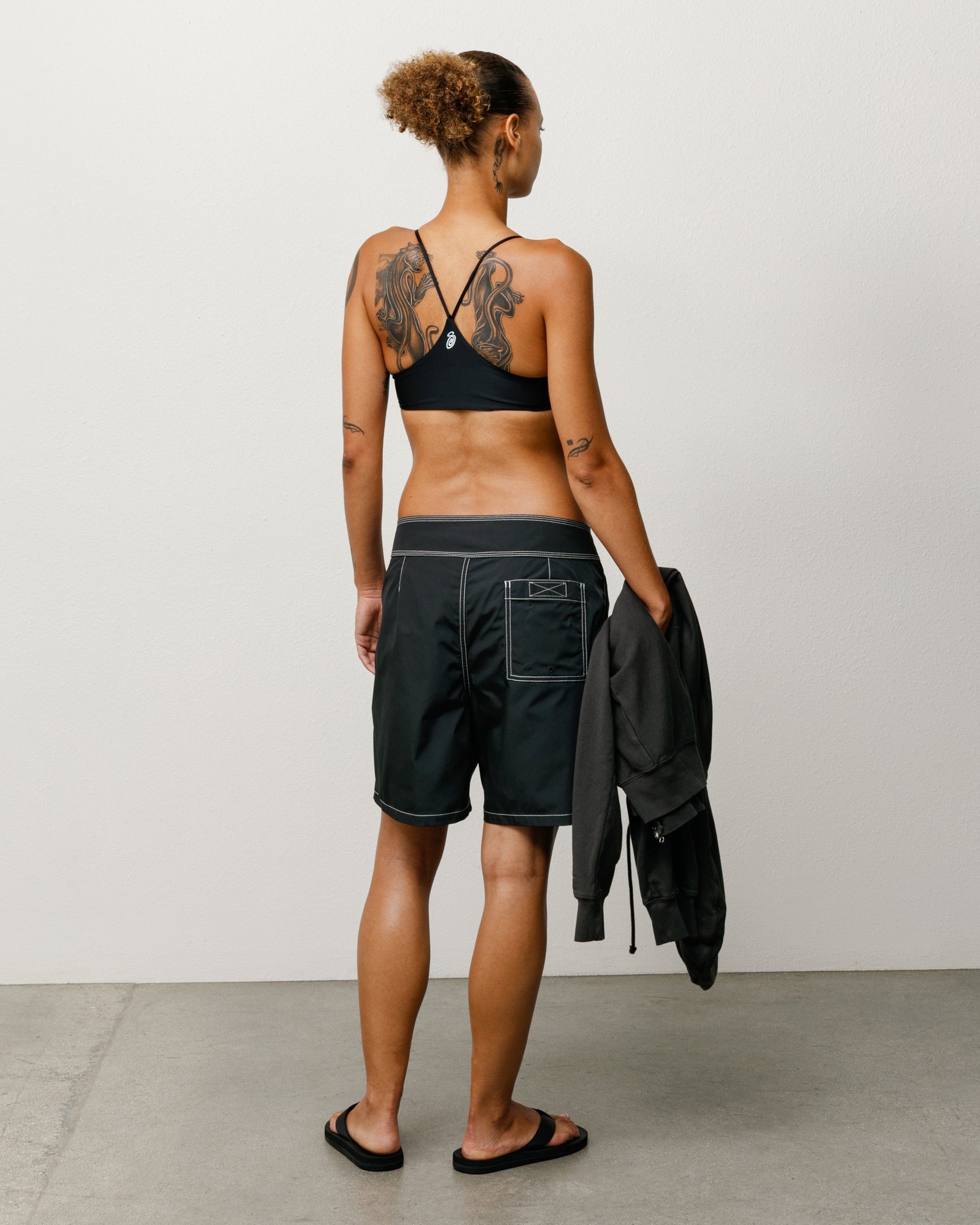 Black unisex board shorts, back view with white contrast stitching and rear patch pocket