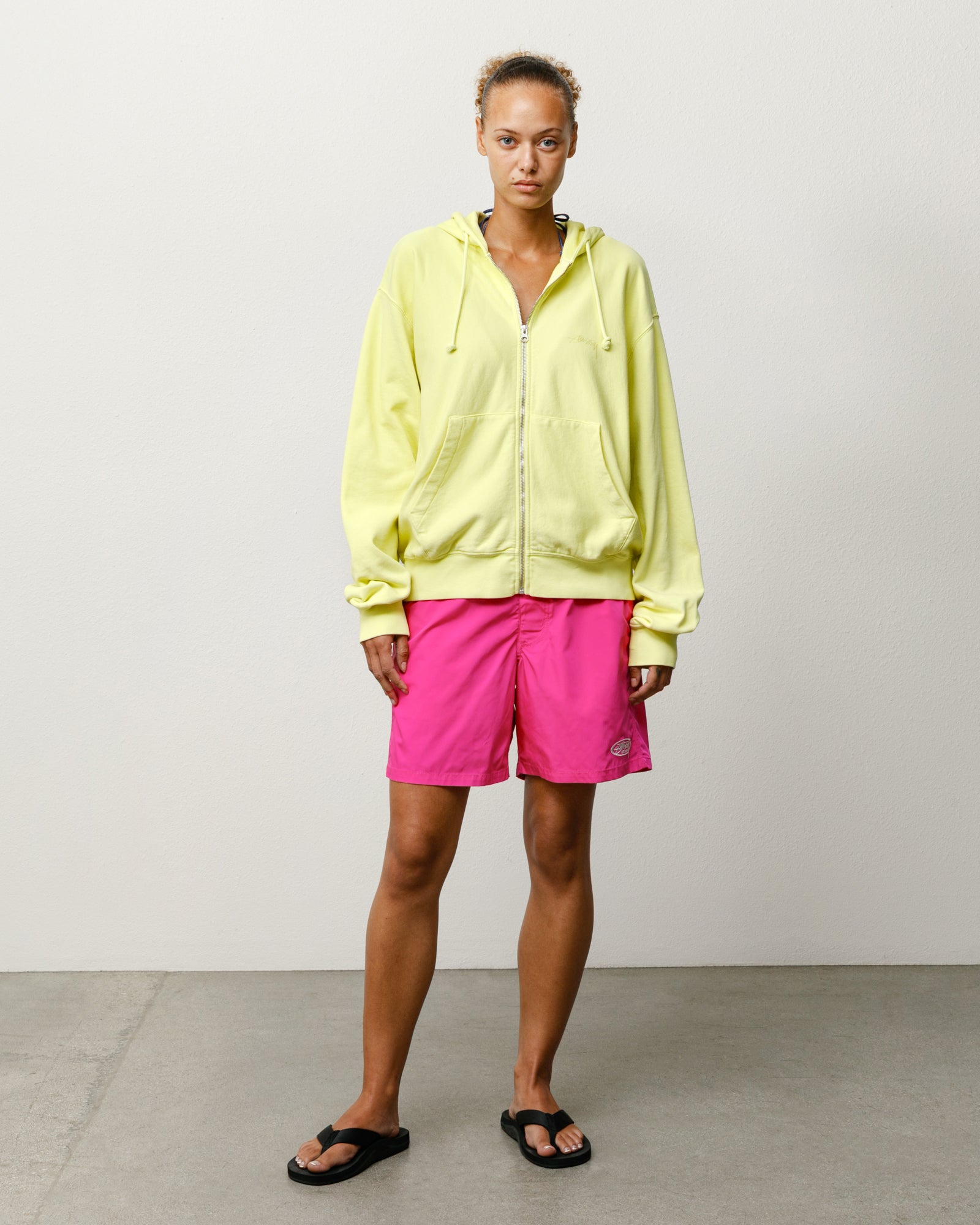 Pink unisex board shorts styled on-model, above-knee length with small logo at left hem.