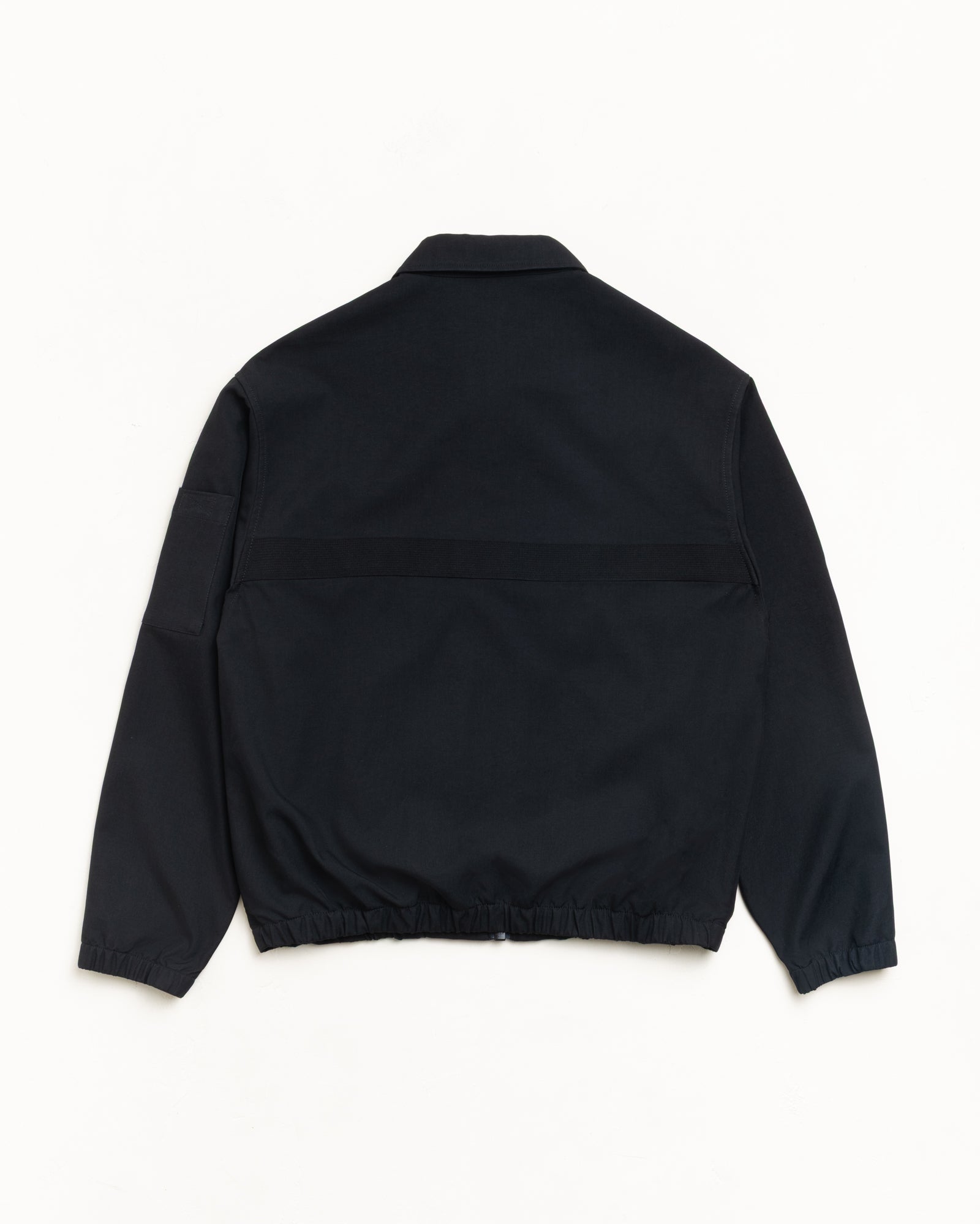 Back view of unisex black mechanic jacket, long-sleeve with horizontal webbing, sleeve pocket, elastic hem