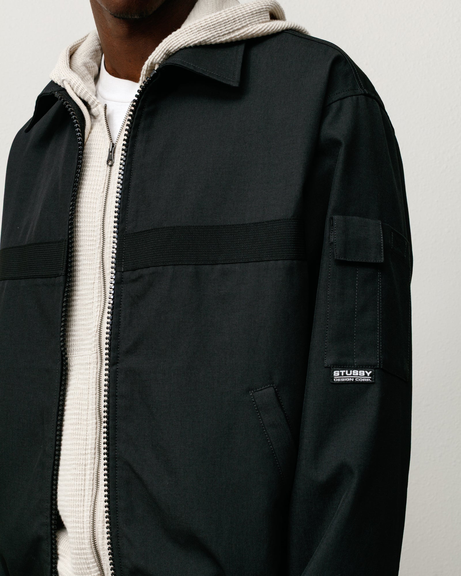 Black mechanic jacket with zip front, angled welt pockets, and sleeve patch label