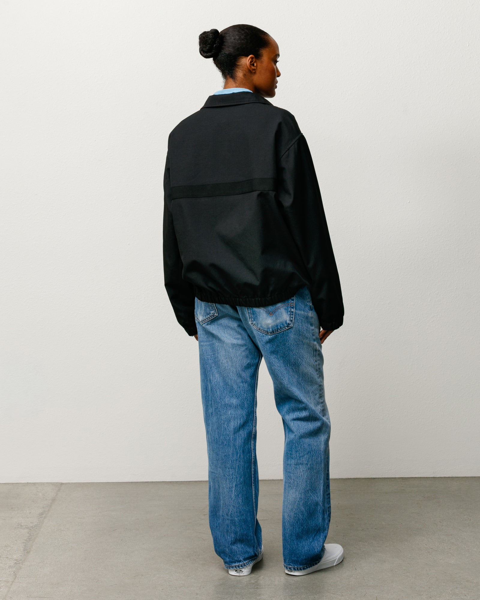Black lightweight jacket on model, back view with webbing detail, elastic hem, and long sleeves