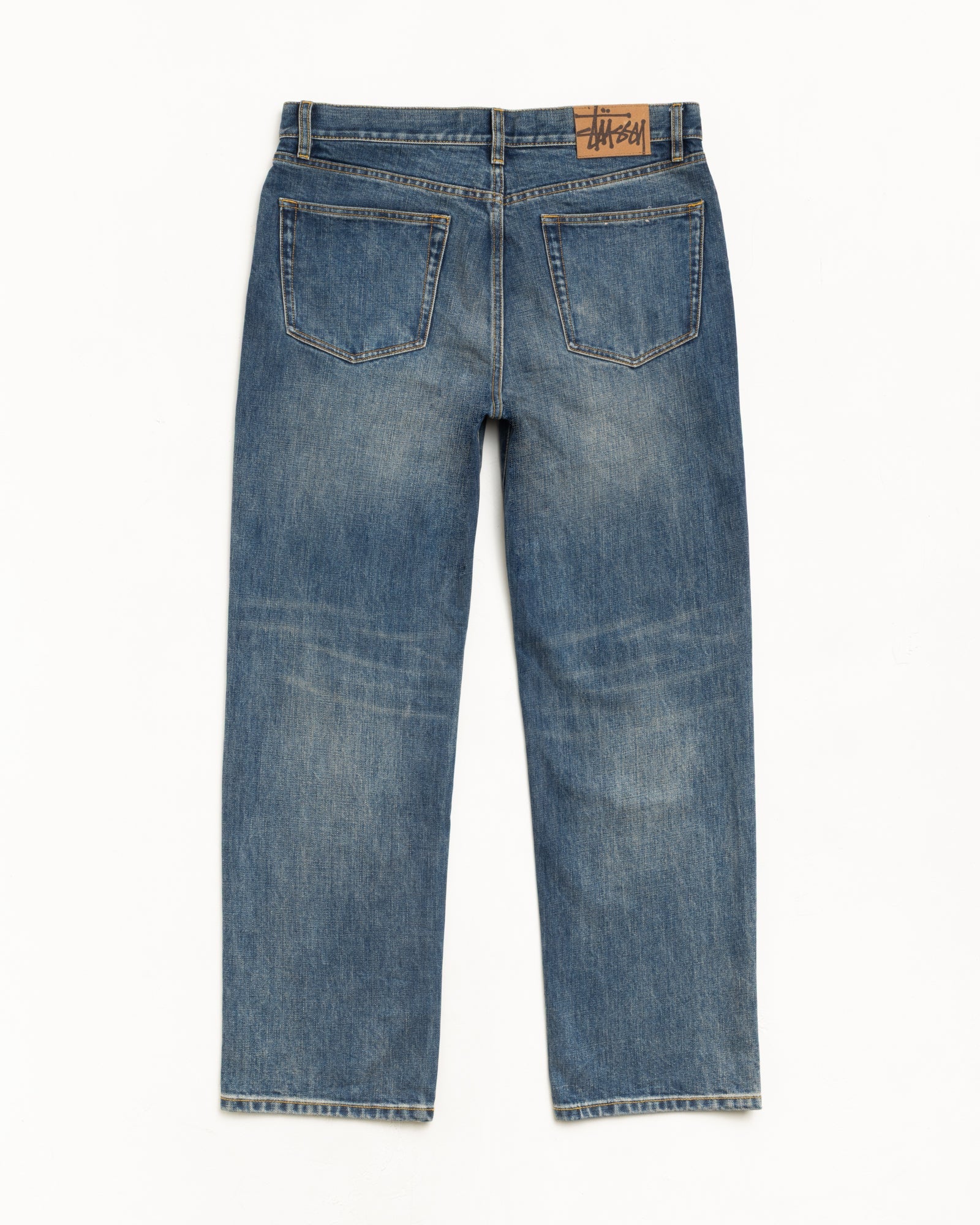 Blue slub denim jeans, back view; straight leg with classic fit and suede Stüssy logo patch at waistband.