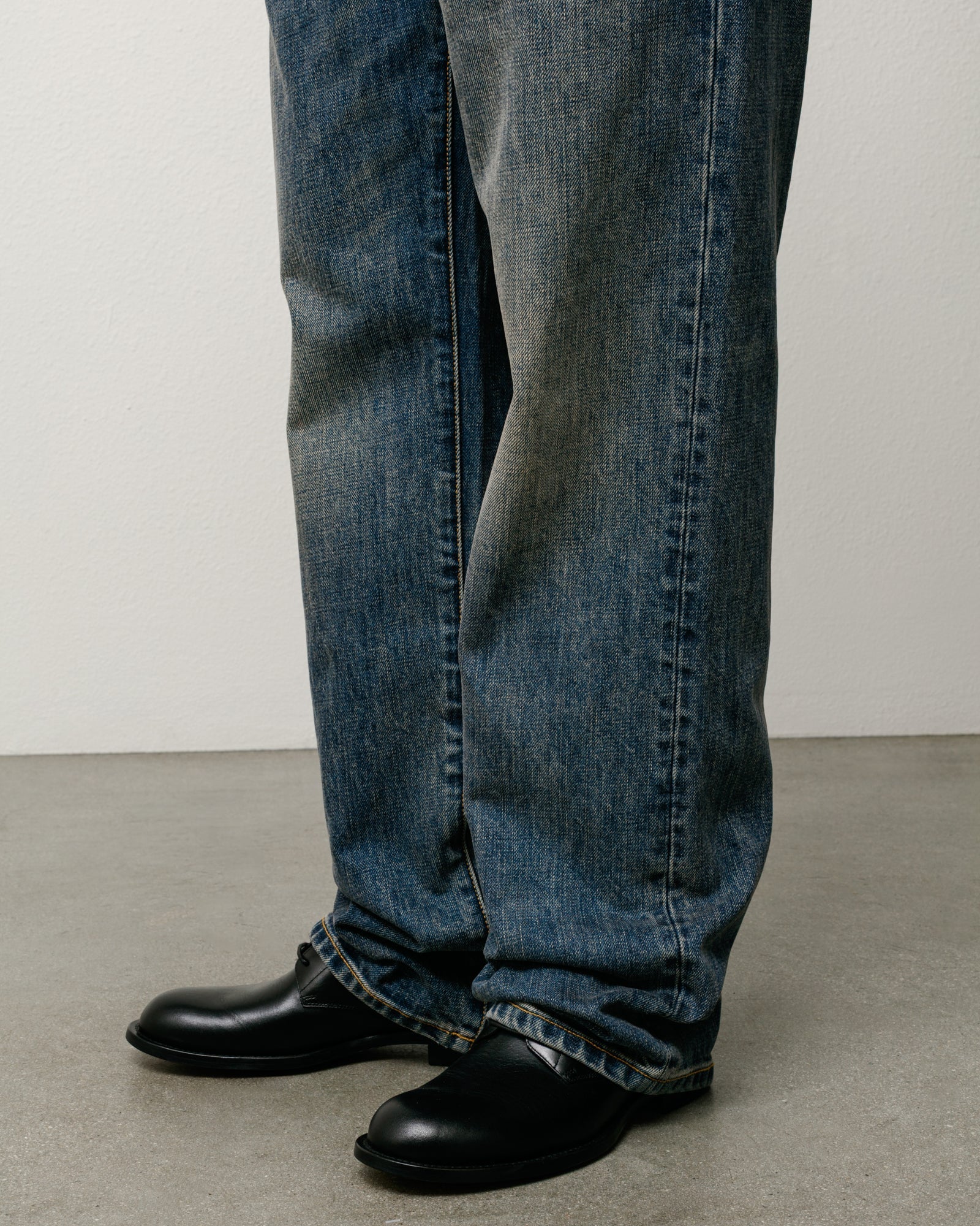 Blue slub denim jeans with a straight-leg fit, worn on model with stacked hems.