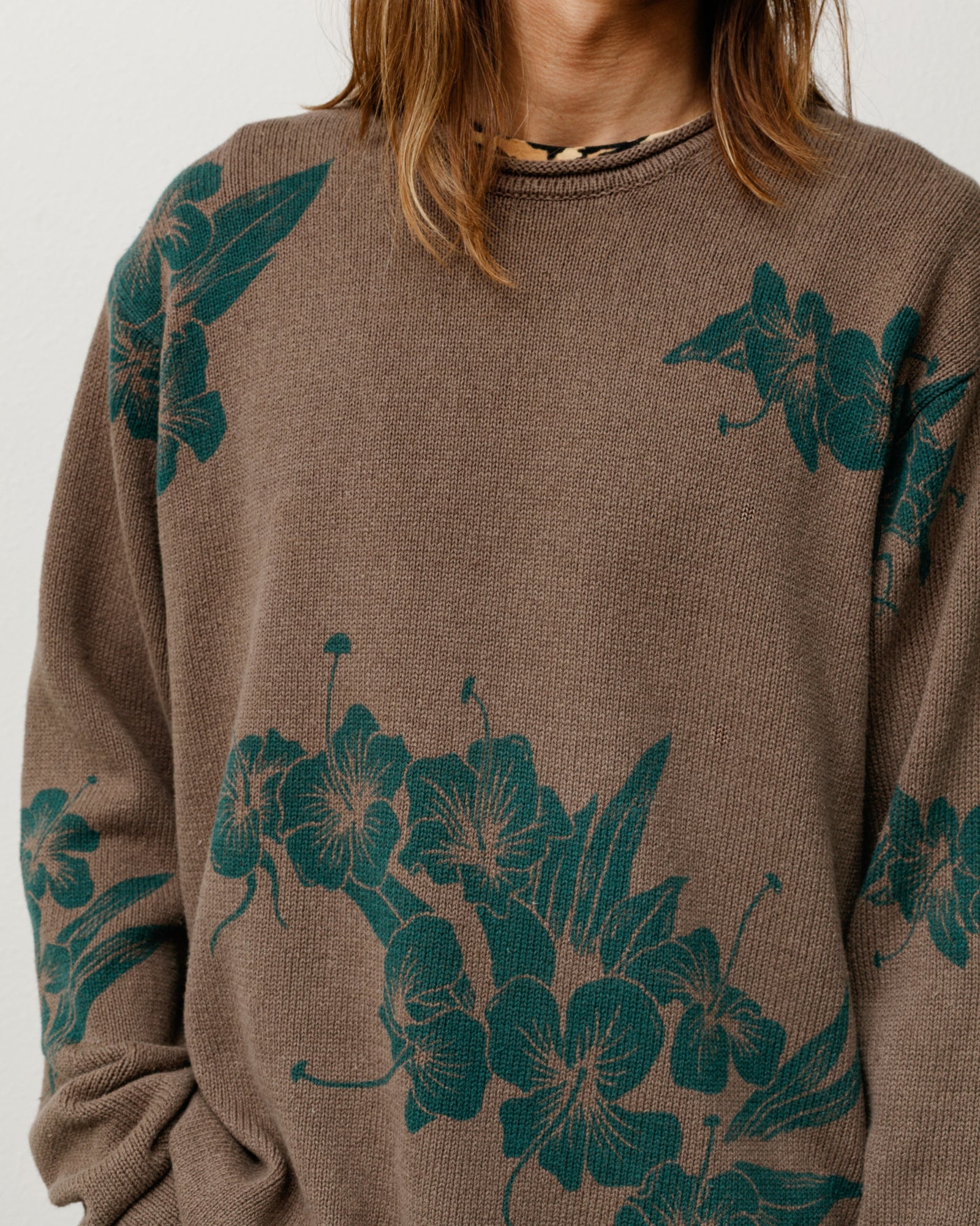 Brown knit sweater with green floral pattern, rolled crewneck, long sleeves, close-up torso.