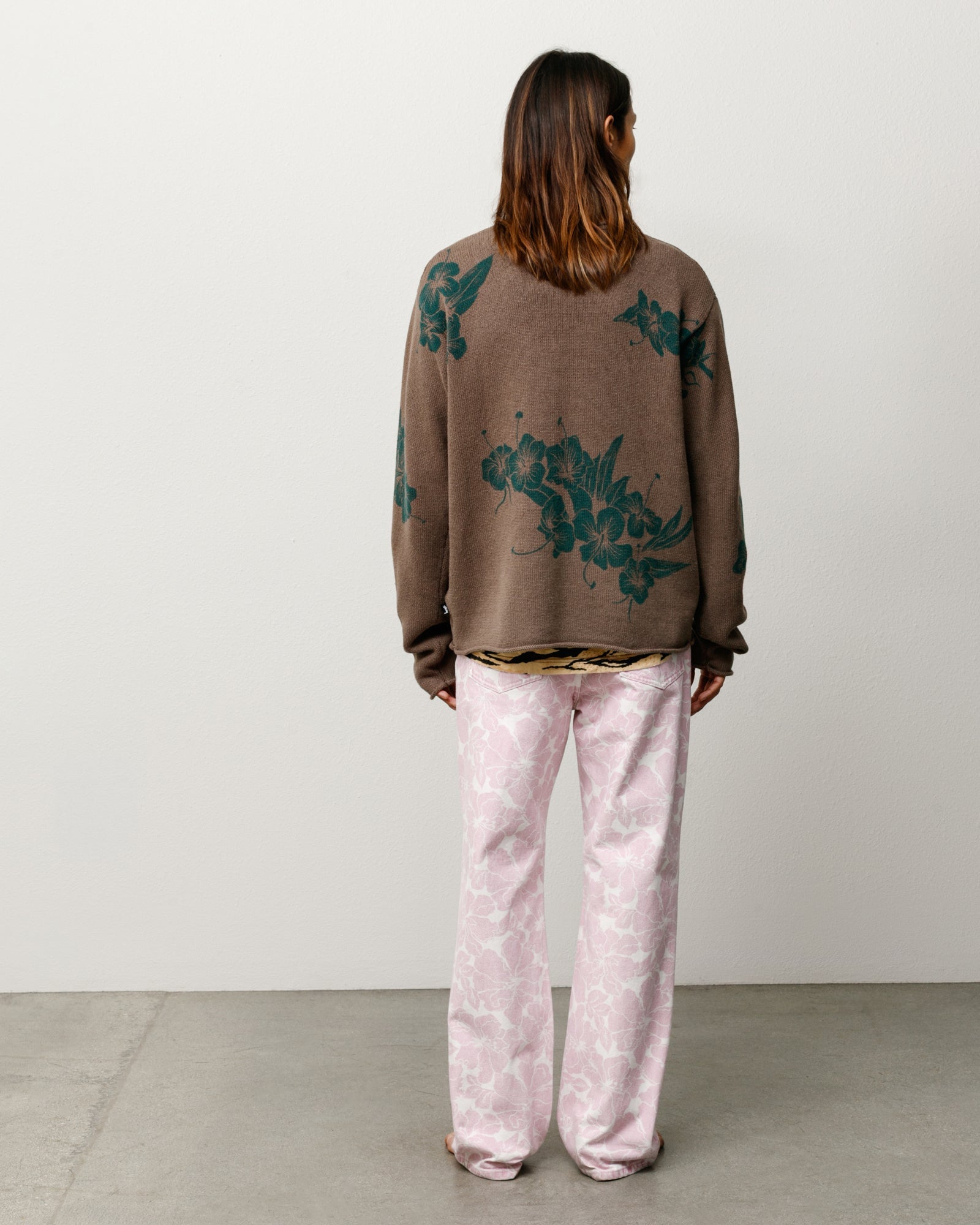 Back view of a brown knit sweater with green floral print, relaxed fit on model