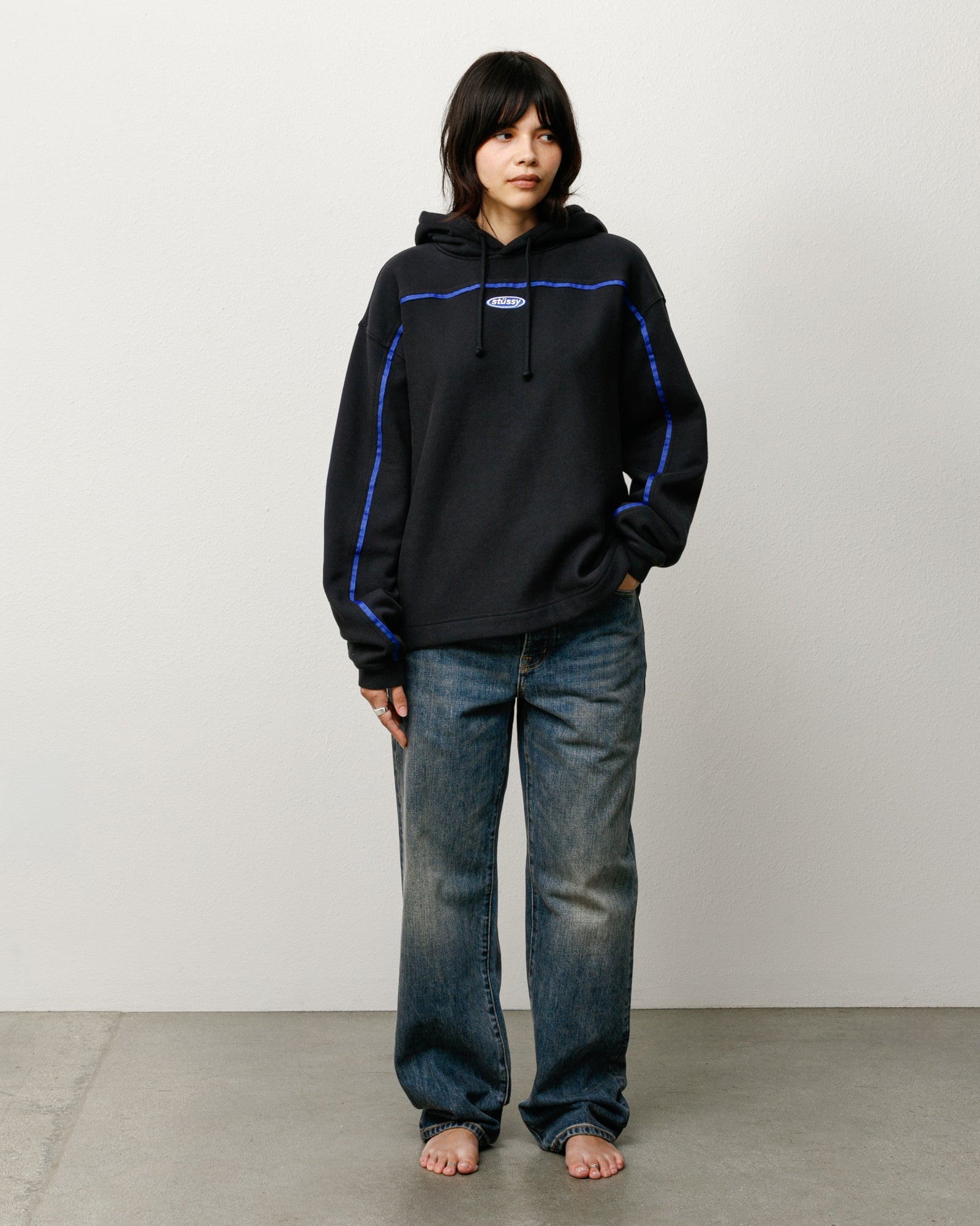 Black unisex pullover hoodie with oval logo, blue seam piping and drawcords, relaxed fit.