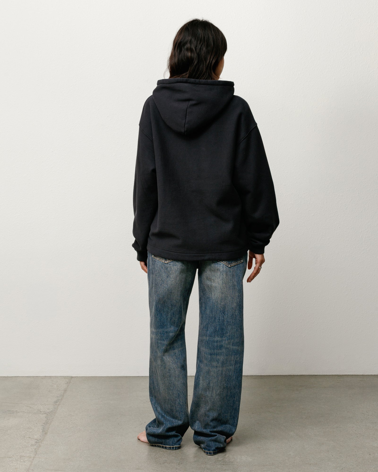 Black unisex pullover hoodie, back view on model; relaxed fit with roomy hood.