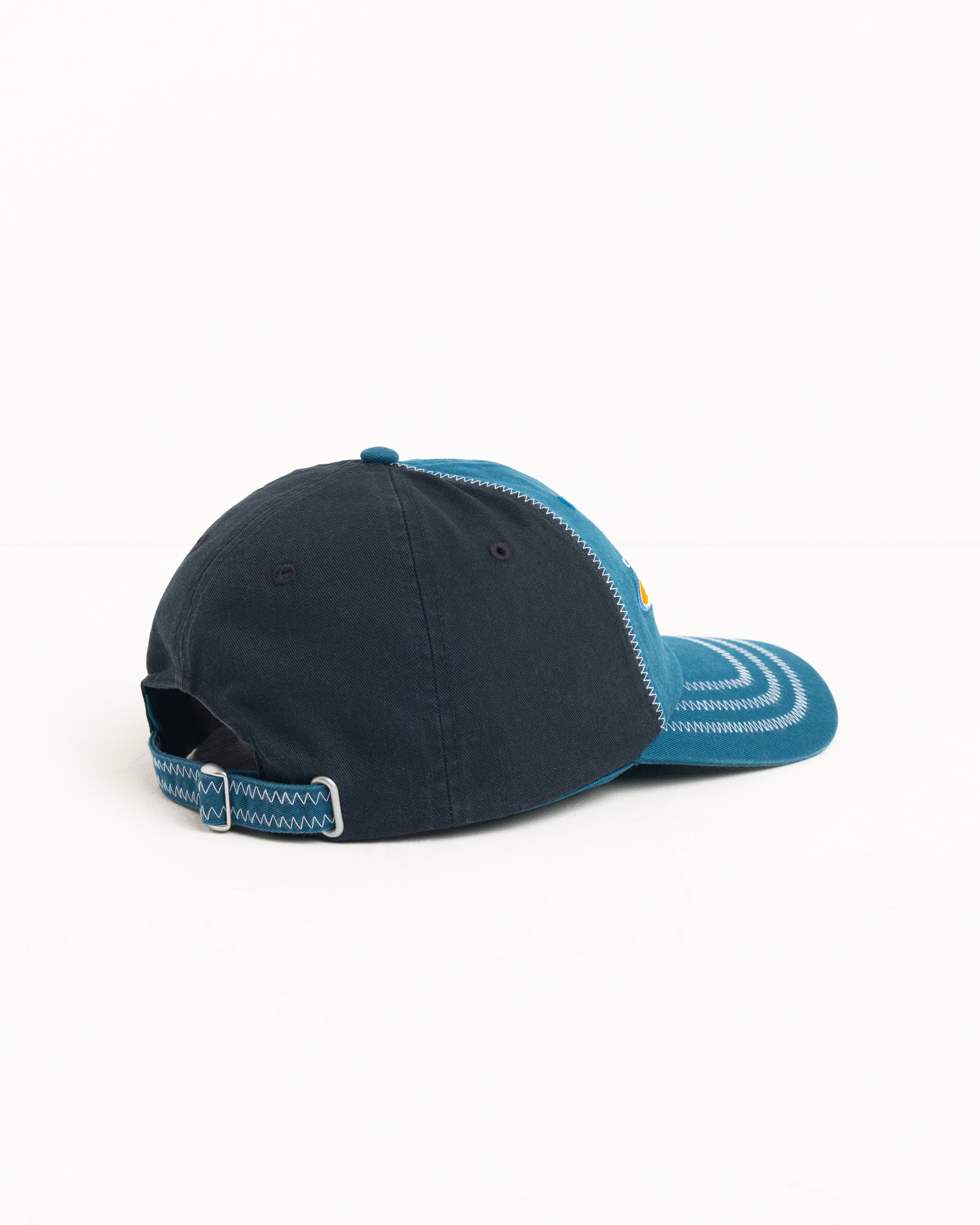 Blue low-profile six-panel cotton twill cap with precurved brim, strapback, and contrast zig-zag stitching