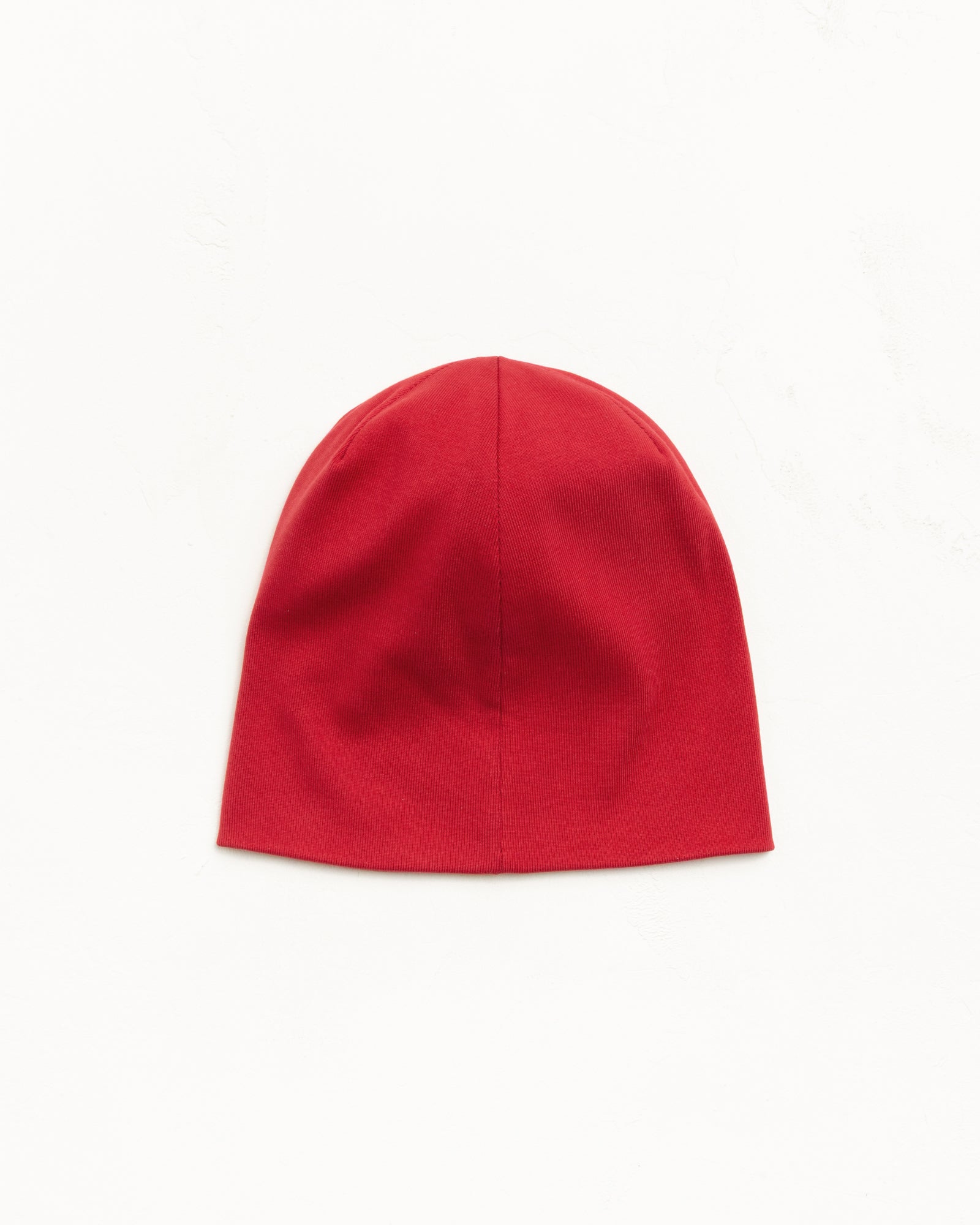 Jersey skullcap beanie in red, fitted unisex style, flat lay on white