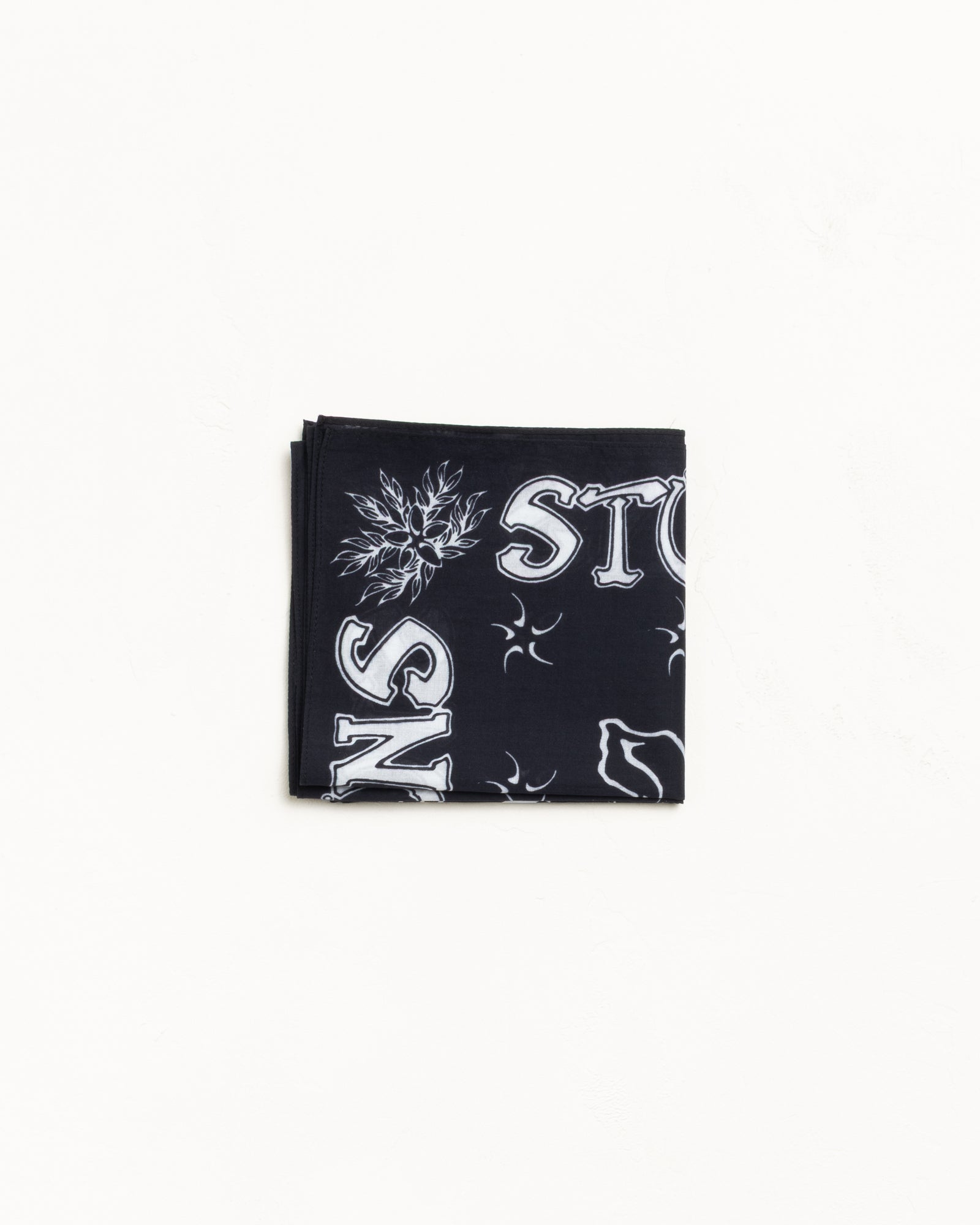 Black cotton bandana with white graphic print, neatly folded flat on a white surface.