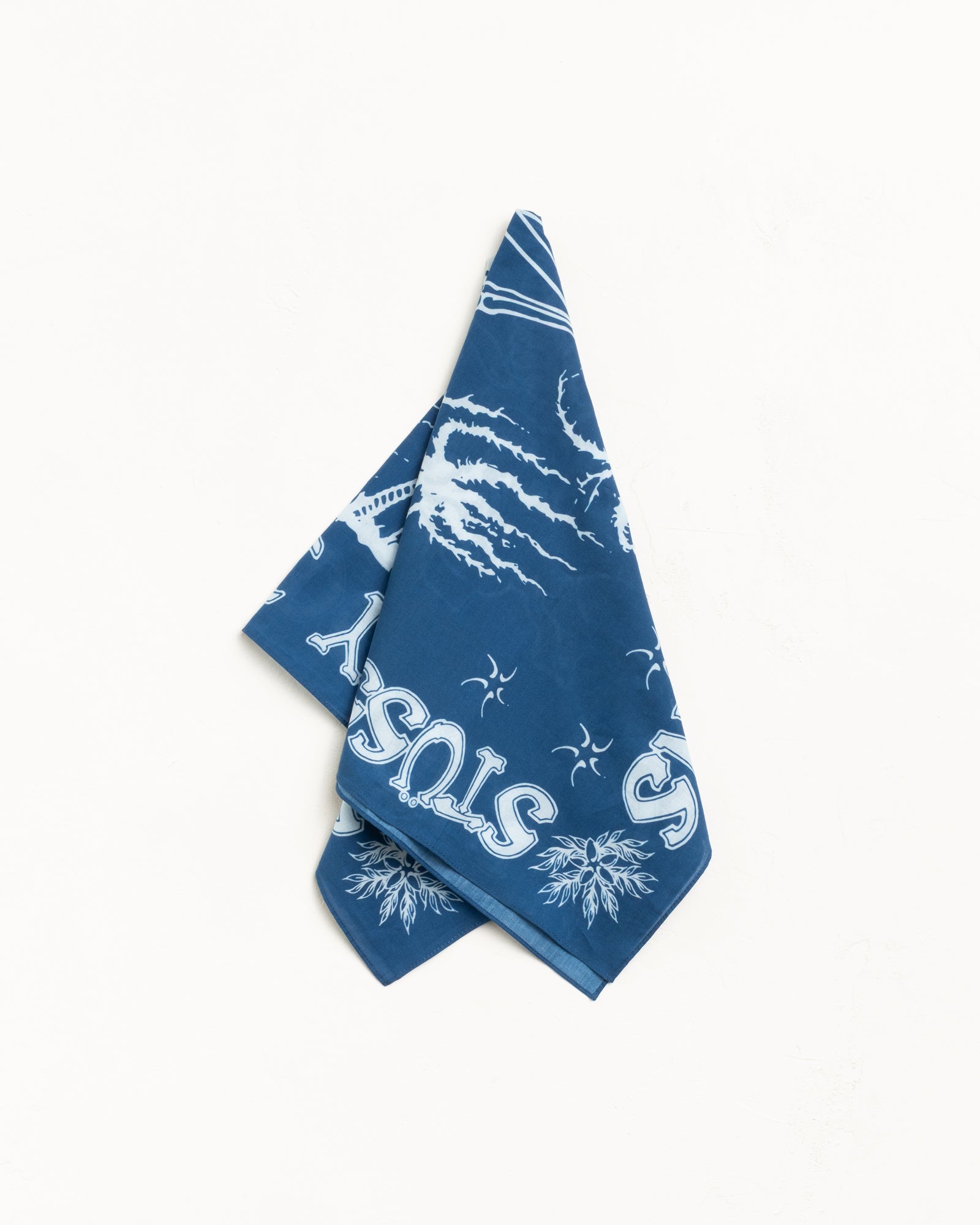 Blue bandana with white graphic print and Stüssy logo, folded on a plain backdrop