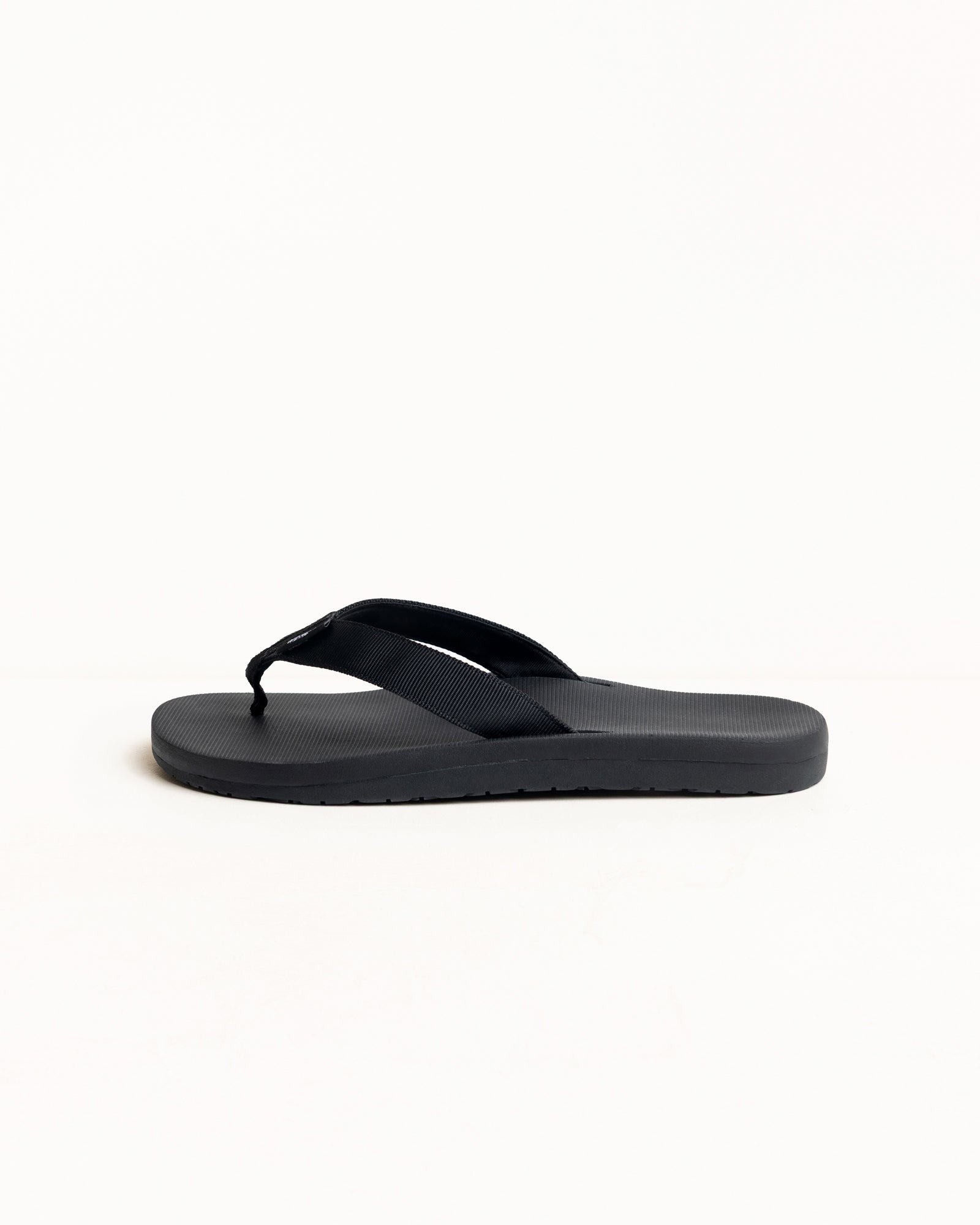 Black rubber flip-flop with wide fabric straps and textured sole, side profile