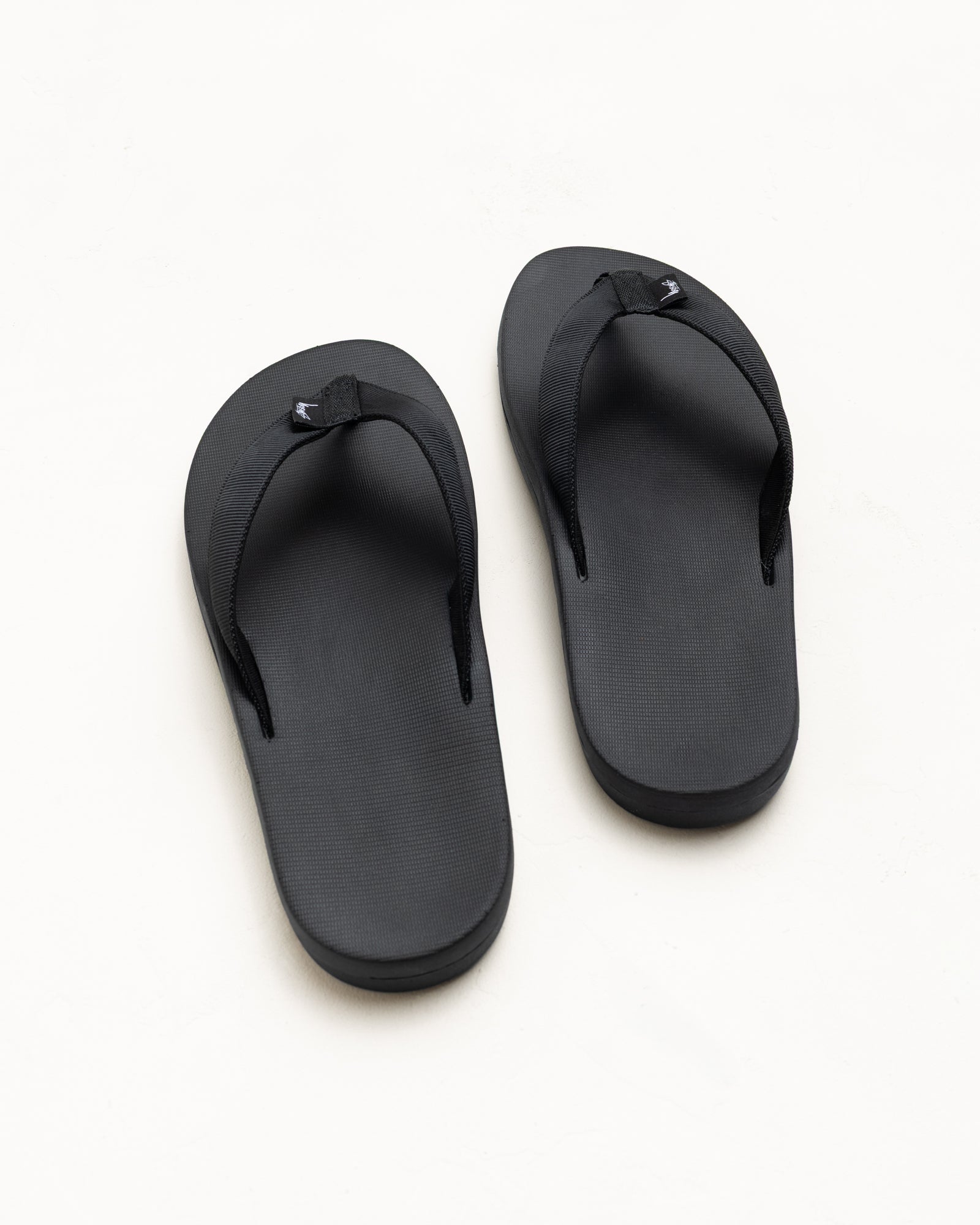 Black rubber unisex flip-flops with wide nylon webbing straps, top view on a white background.