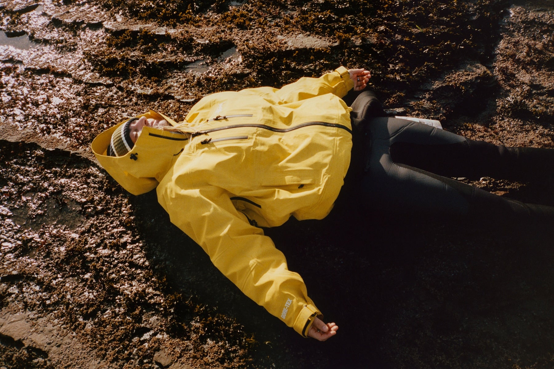 Person laying on rocks wearing yellow gore-tex jacket