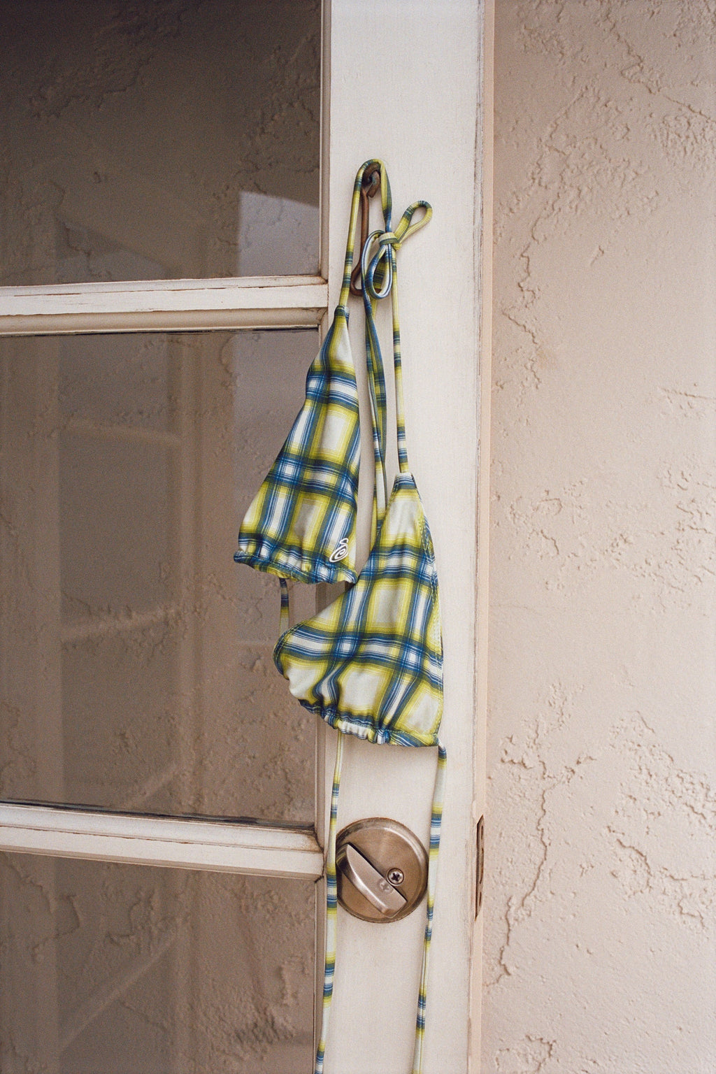Triangle Bikini Top in Green Plaid hanging from a latch on a weathered white door.